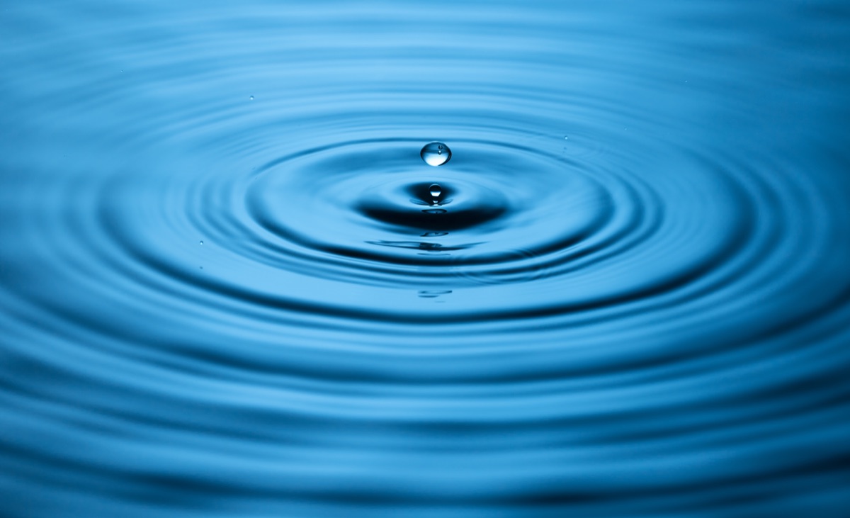 A water drop rebounding from a still blue surface, sending out concentric ripples