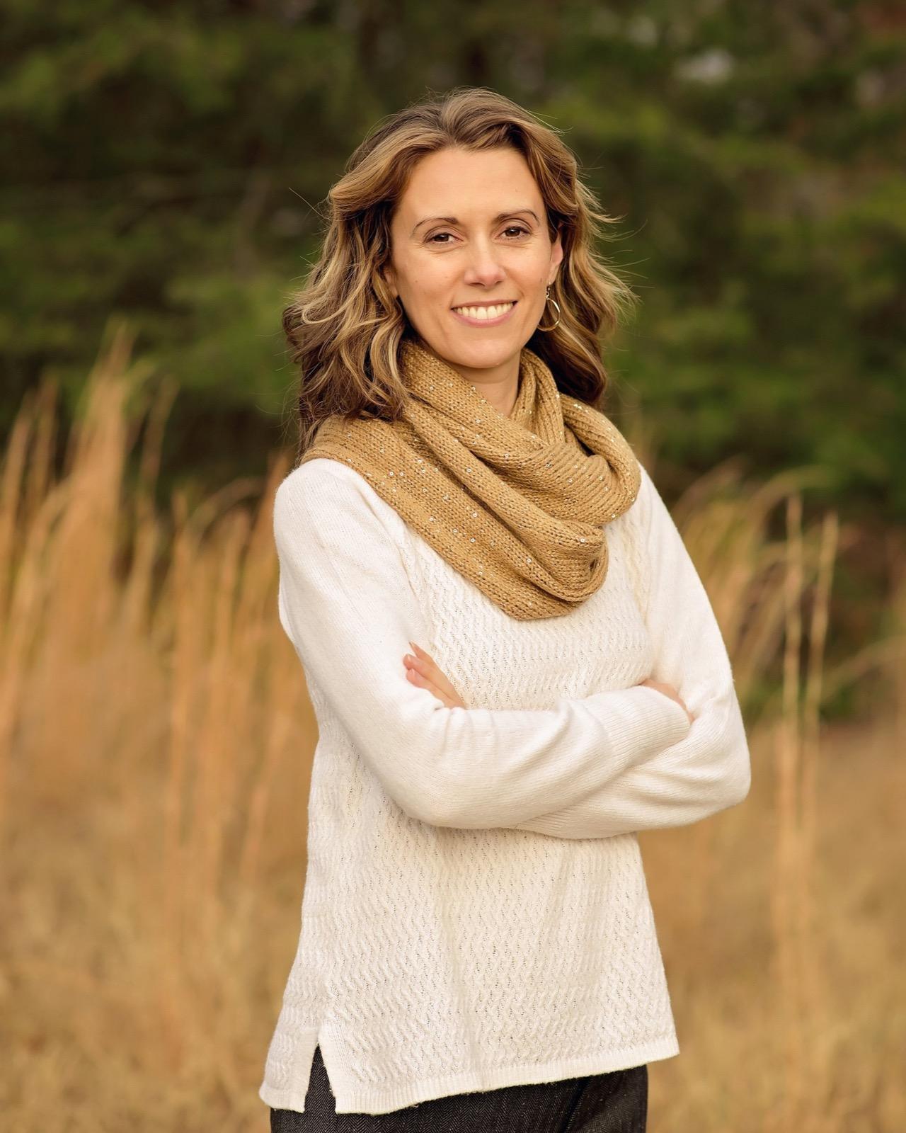 Meg Simmons standing in a golden field, arms crossed, smiling