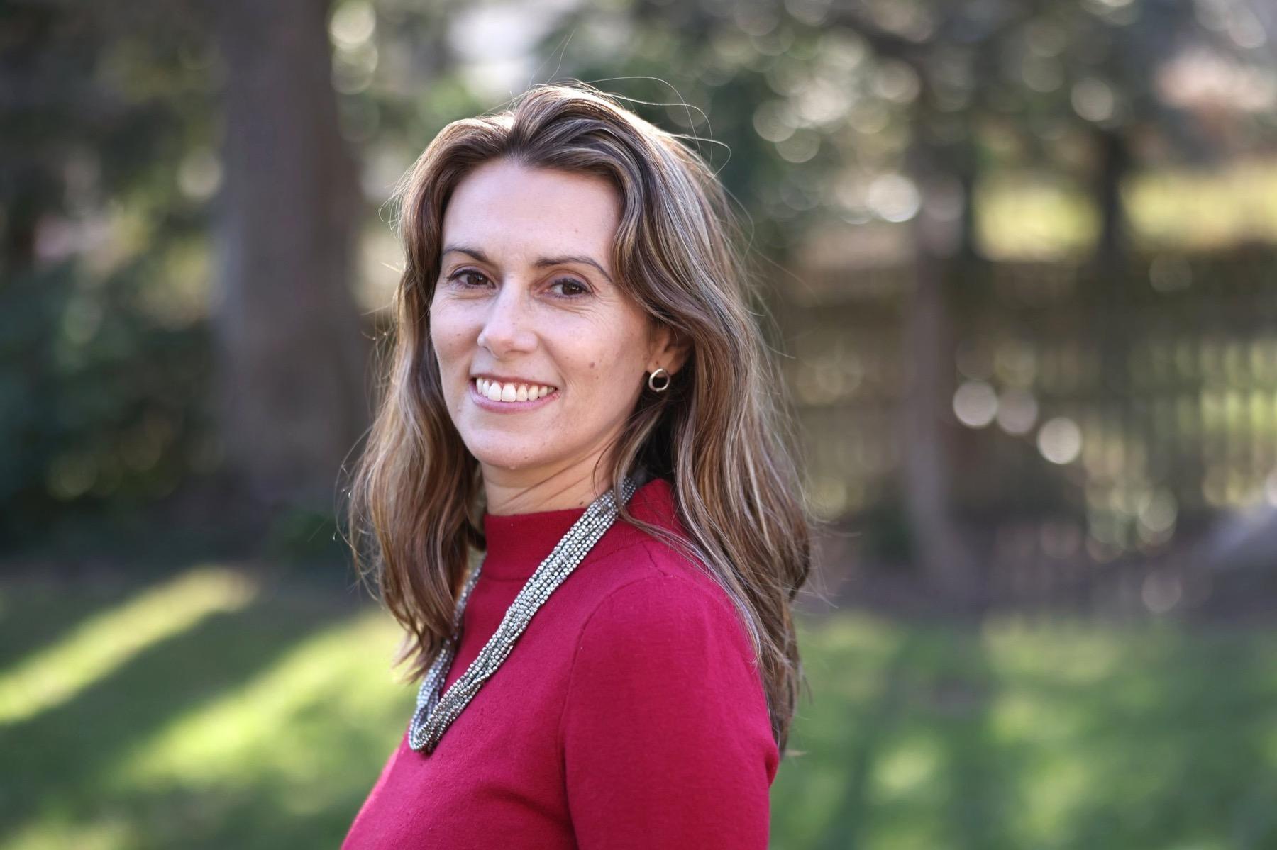 Meg Simmons outdoors in a red sweater, smiling over her shoulder