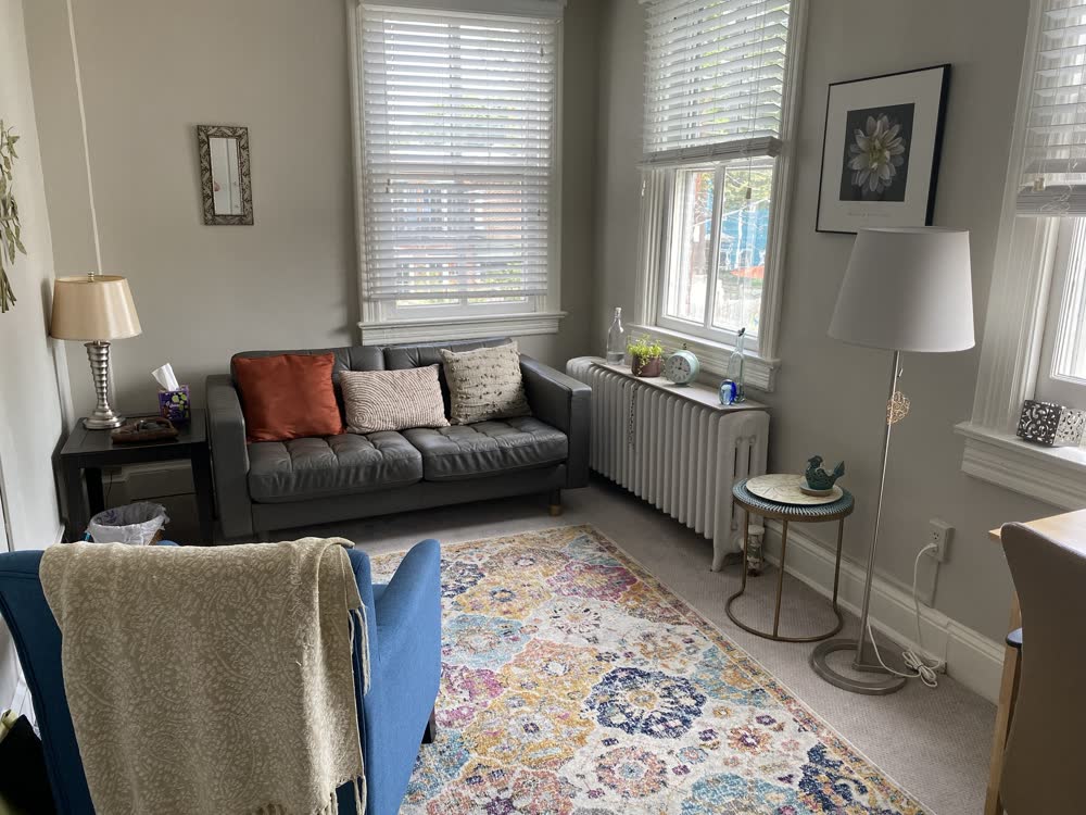 Meg's therapy office with a gray sofa, warm pillows, and a colorful rug
